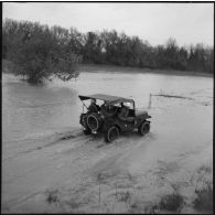 Des soldats patrouillent en jeep sur un chemin inondé près de Bône, le jour de la visite du secrétaire d'état Max Lejeune et du général Salan.