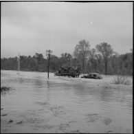 Une jeep de l'armée, avec à son bord des officiers généraux et des soldats, remorque une Citroën traction sur un chemin inondé.