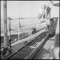 Un matelot charpentier aplanit au rabot l'échelle de coupée lors d'un exercice à bord de l'escorteur Hova.