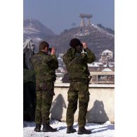Du toit de la Compagnie de renfort opérationnel (CRO), des militaires danois surveillent Mitrovica à l'aide de jumelles.