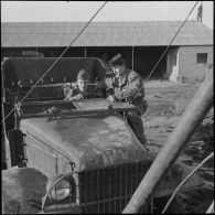 Deux militaires posent auprès d'un véhicule GMC CCKW 353 dont l'une des deux vitres du pare-brise est cassée.