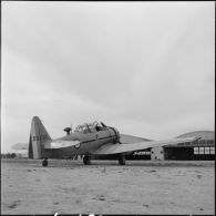 Un avion North American T6 devant des hangars.