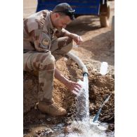 Un technicien vétérinaire prélève de l'eau à la sortie d'un tuyau pour un contrôle à Ménaka, au Mali.