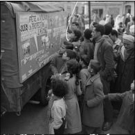 Groupement de population civile devant un camion radio et de propagande.
