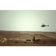 En ZDO (zone de déploiement opérationnel) Olive, un hélicoptère américain de reconnaissance et d'observation Bell-OH58 Kiowa muni d'un système de visée pour la lutte antichar monté sur mat au-dessus du rotor survole un camion du 1er RS (régiment de spahis) posté dans le désert.