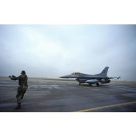 Un mécanicien de piste américain guide un avion de combat F-16 sur la piste de la base américaine de CRK (camp du roi Khaled).