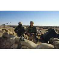 Au campement américain de la 82e Airborne en ZDO (zone de déploiement opérationnel) Olive, deux militaires font le guet derrière un abri de sacs de sable, munis de jumelles et armés de fusils d'assaut M16.