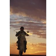 En ZDO (zone de déploiement opérationnel) Olive, une estafette réalise une roue arrière sur sa motocyclette Cagiva 350 cm3 dans le soleil couchant.