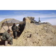 En ZDO (zone de déploiement opérationnel) Olive, un groupe de soldats américains prend son repas au pied d'un transport de troupes M-113, sous un filet de camouflage.