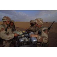 En ZDO (zone de déploiement opérationnel) Olive, autour d'une table supportant des gamelles, des soldats américains perçoivent leur plateau-repas dans le désert.