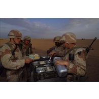 En ZDO (zone de déploiement opérationnel) Olive, autour d'une table supportant des gamelles, des soldats américains perçoivent leur plateau-repas dans le désert.