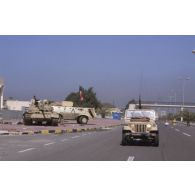 Un véhicule tactique léger koweitienen armé d'une mitrailleuse dépasse un blindé transport de troupes koweitien et un char de combat T-55 irakien abandonné sur une route de Koweit city.