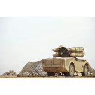 Unité de tir Crotale sur véhicule à roues dans le désert, un filet de camouflage tendu sur son flanc gauche.