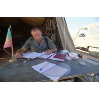 Un lieutenant de la Légion écrit les ordres du jour, assis à son bureau devant sa tente.