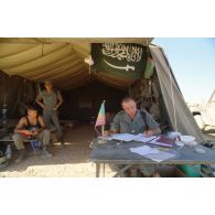 Un lieutenant de la Légion étrangère écrit les ordres du jour, assis à son bureau, devant une tente.