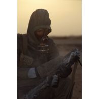 Un soldat du du 1er RI en tenue S-3P (survêtement de protection à port permanent) et portant l'ANP (appareil normal de protection) nettoie son fusil d'assaut FAMAS à l'aide d'un gant de décontamination chimique d'urgence lors de l'exercice NBC.