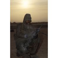 Un soldat du 1er RI en tenue S-3P (survêtement de protection à port permanent) et portant l'ANP (appareil normal de protection) nettoie son fusil d'assaut FAMAS à l'aide d'un gant de décontamination chimique d'urgence lors de l'exercice NBC.