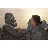 Un soldat en tenue S-3P (survêtement de protection à port permanent) et portant l'ANP (appareil normal de protection) nettoie le visage de son camarade à l'aide d'un gant de décontamination chimique d'urgence lors de l'exercice NBC du 1er RI.