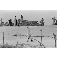 Des hommes tchadiens devant des pirogues au bord de l'eau.