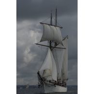 La Belle-Poule, voilier-école de la Marine nationale, navigue sous le vent, sous un ciel chargé de la ville de Brest.
