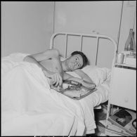 Un sergent du 8e bataillon de parachutistes coloniaux (8e BPC) blessé à Diên Biên Phu et rapatrié à l'hôpital Grall de Saigon se repose dans un lit.