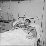 Un sergent du 2e bataillon étranger de parachutistes (2e BEP) blessé à Diên Biên Phu et rapatrié à l'hôpital Grall de Saigon prend un repas dans son lit.