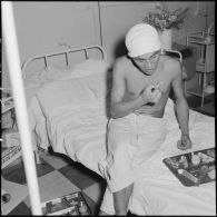Un soldat de 2e classe du 1er bataillon du 2e régiment étranger d'infanterie (1/2 REI) blessé à Diên Biên Phu et rapatrié à l'hôpital Grall de Saigon prend un repas dans son lit.