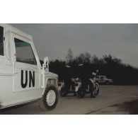 Deux motards de dos et une Peugeot P4 en tête d'un convoi de véhicules aux couleurs de l'ONU lors d'une démonstration à la presse avant le départ pour la FORPRONU.