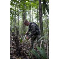 Un stagiaire coupe une feuille de palmier pour réaliser un abri feu sur un bivouac en zone d'instruction de Tuff, en Guyane française.