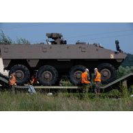 Des soldats du centre de coordination interarmées des transits, transports et mouvement (CCITTM) ôtent les cales sous les roues d'un véhicule blindé de combat d'infanterie (VBCI) à Voila, en Roumanie.