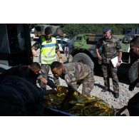 Des prévôts encadrent l'évacuation d'un blessé par le personnel du Service de santé des armées (SSA) à bord d'une ambulance vers l'hôpital civil de Brasov depuis le Rôle 1 de Cincu, en Roumanie.
