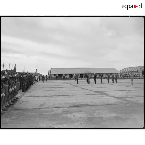 Plan d'ensemble d'une cérémonie militaire, sur un aérodrome, à laquelle assiste le général Philippe Leclerc, accompagné d'autorités militaires.