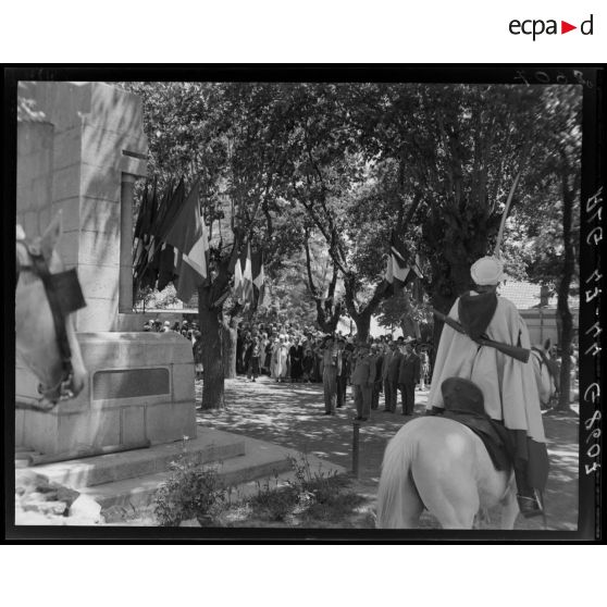 Des autorités civiles et militaires, parmi lesquelles le général Duché, saluent devant le monument aux morts de Teniet El Had, sous le regard de la population civile.