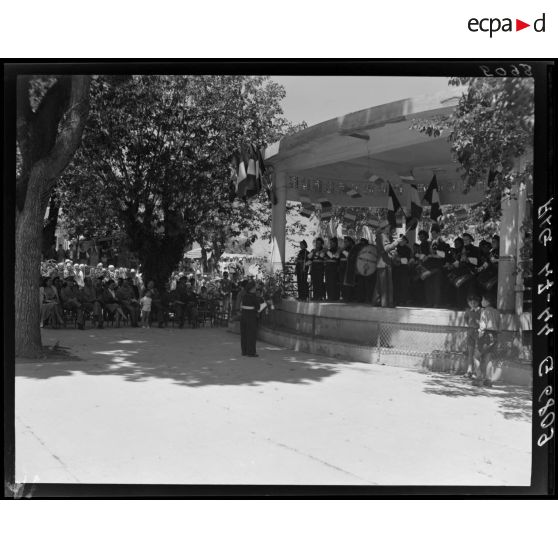 La musique militaire d'une unité d'enfants de troupes donne un concert dans un kiosque à musique, sous le regard d'autorités civiles et militaires.