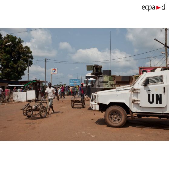 Un VAB français et un FAV (fast attack vehicle ou véhicule d'attaque rapide) blindé Stanag-1 Black Scorpion, équipant la police rwandaise aux couleurs de l'ONU, stationnent au checkpoint tenu par le SGTIA Gris et la MINUSCA à Bangui devant le bâtiment de la brigade de gendarmerie territoriale de PK 12, à l'entrée d'une zone de marché. Une affiche incite à la prévention des MST.