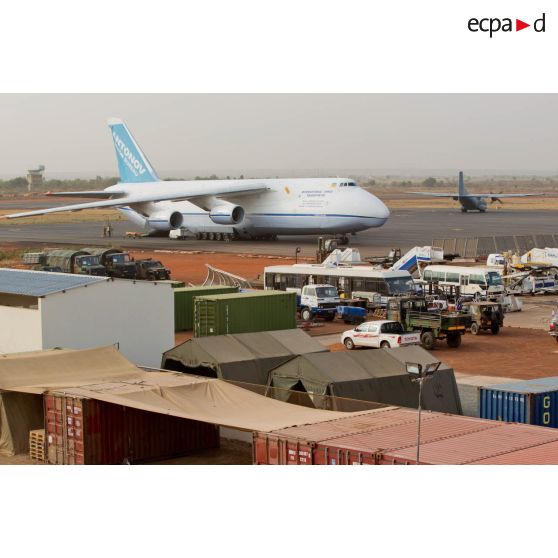 Derrière une zone de regroupement logistique, un avion-cargo de transport Antonov 124-100 ukrainien stationne sur une piste de l'aéroport de Bamako, pendant le roulage d'un Transall C-160 français.