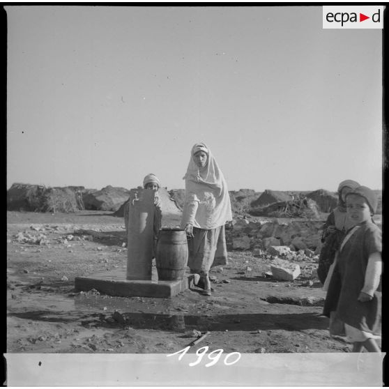 Aménagement de l'eau dans le secteur de Tamesna sous le commandement du capitaine Vinck. Une jeune femme venue remplir un tonneau d'eau potable. Trois jeunes enfants sont également présents à proximité du point d'eau. [légende d'origine]