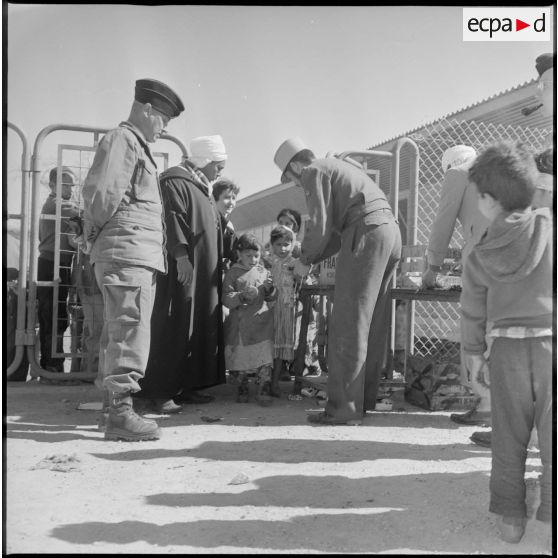 Devant un bâtiment, des soldats effectuent une distribution auprès des enfants de Wagram. [légende d'origine]