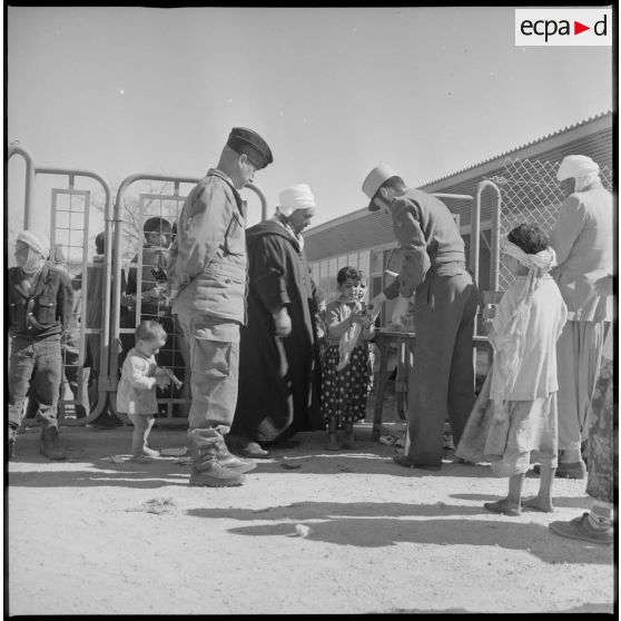 Devant un bâtiment, des soldats effectuent une distribution auprès des enfants de Wagram. [légende d'origine]