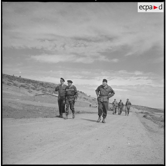 Quelques soldats marchent sur une route. En arrière-plan, sur la gauche, une bâtisse. André Wormser. [légende d'origine]