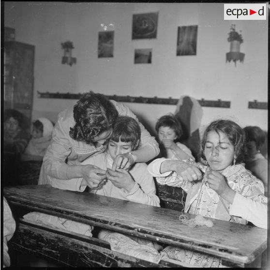 Apprentissage professionnel. Dans une salle de classe, une enseignante s'occupe de l'apprentissage du tricot auprès de ses jeunes élèves. [légende d'origine]