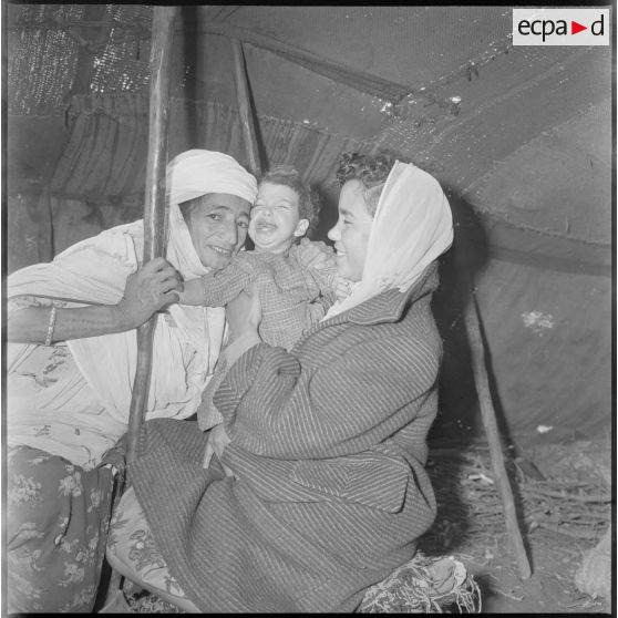 Portrait d'une membre d'une EMSI, d'une femme et d'une jeune enfant à l'intérieur d'une khaïma au cours d'une séance d'auscultation. [légende d'origine]