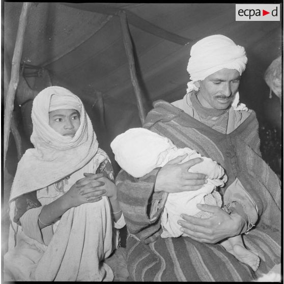 Portrait d'un homme, d'une femme et de leur bébé à l'intérieur d'une khaïma. Ils attendent leur tour pour faire ausculter leur enfant. [légende d'origine]