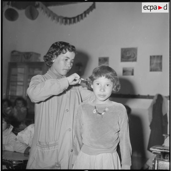 Apprentissage professionnel. Dans une salle de classe, une jeune élève est coiffée par une enseignante. [légende d'origine]