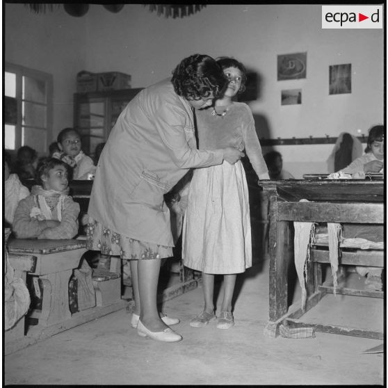 Apprentissage professionnel. Dans une salle de classe, après avoir été coiffée par une enseignante, une jeune élève essaye les vêtements cousus par ses camarades. [légende d'origine]