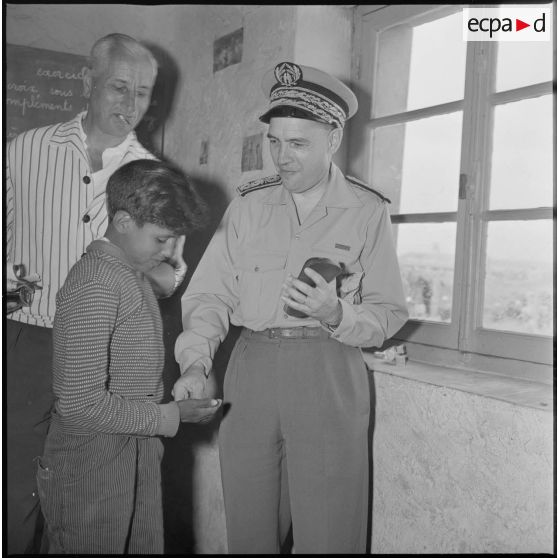 En visite dans une école du secteur de Saïda, le préfet du département, monsieur de Solmignac, distribue quelque chose à un écolier. [légende d'origine]