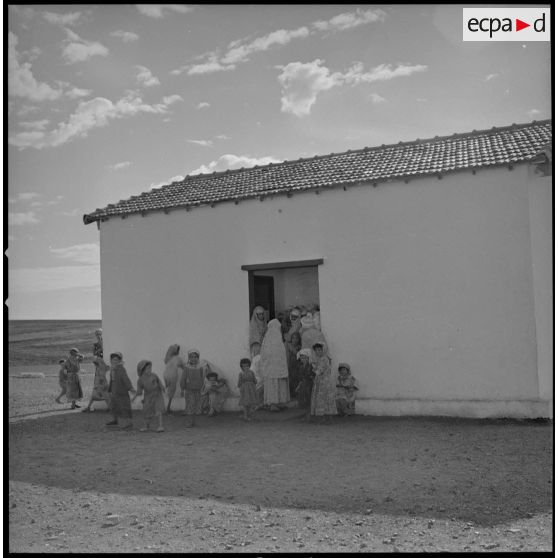 [Des femmes et des enfants attendent devant une bâtisse. Ils viennent au centre de soin pour une visite médicale effectuée par un médecin militaire provenant des SAS.]