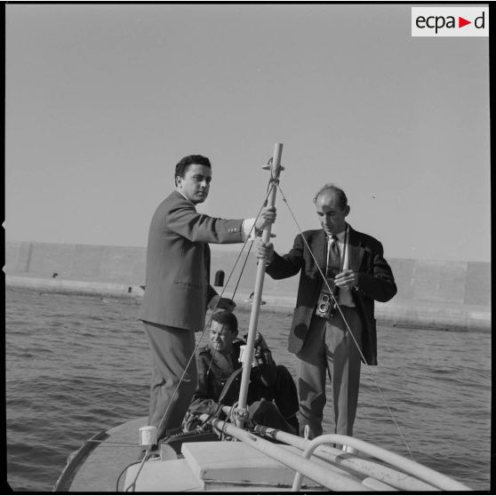 [Un caméraman aux Armées, un photographe et un journaliste tenant le mat d'une embarcation à Oran.]