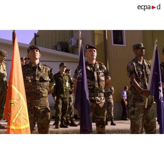 Trois porte-drapeaux de la cérémonie : drapeau du CINC-SOUTH (commandement en chef des forces alliées d'Europe du sud) en rouge, porté par un soldat espagnol, et drapeaux de l' OTAN et de la KFOR.