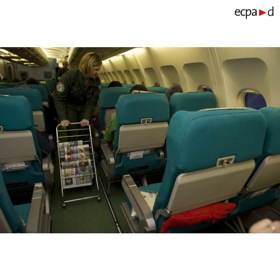 Un personnel féminin de cabine propose des journaux français (L'Equipe, Le Figaro, Le Monde) aux ressortissants évacués de Tripoli (Libye) dans l'avion Airbus A340 de l'escadron de transport 3/60 Esterel.